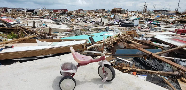 A child’s pink tricycle sits on a concrete slab in front of a wide field of wreckage where homes once stood.